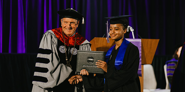MGA's President Blake posing with a student in graduation regalia.